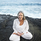 Older woman in lotus pose by the sea