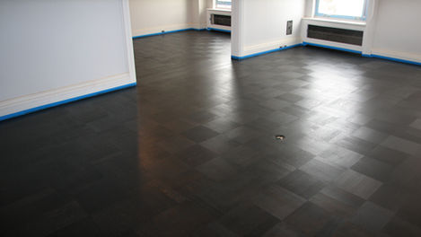 Freshly installed ebonized wood parquet flooring in a New York residence, with the basket-weave block pattern catching light at varying angles, baseboards taped for protection, by I.J. Peiser's Sons.