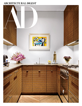 Architectural Digest cover featuring a compact contemporary kitchen with richly textured wood cabinetry, herringbone flooring, and colorful artwork.


