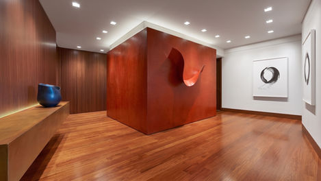 Full view of Wide-Plank Bubinga floors in a New York collector's gallery at night, with vermillion sculpture wall, fluted wood paneling, and museum-quality art, installed by I.J. Peiser's Sons.