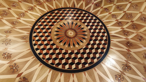 Overhead view of a custom multi-species wood floor medallion with tumbling-block parquet center, floral rosette, and radiating sunburst inlay with botanical motifs, hand-crafted by I.J. Peiser's Sons.