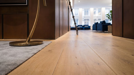 Floor-level detail of wide-plank white oak floors running the full length of a SoHo loft corridor with oiled walnut cabinetry and cast brass lamp base, installed by I.J. Peiser's Sons.