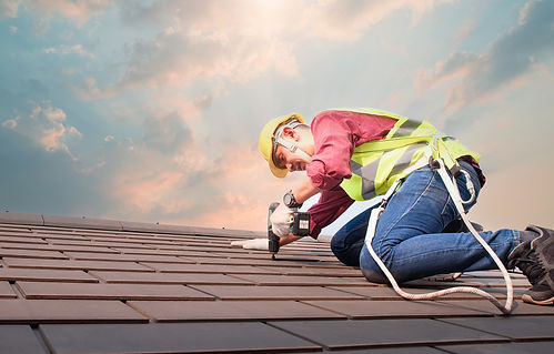Roofer working on dark shingles under a cloudy sky.