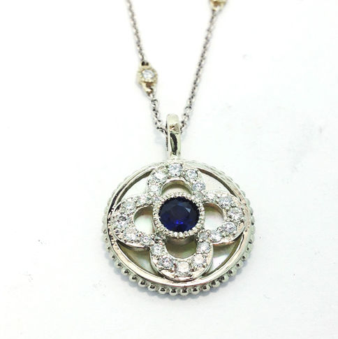Sapphire and diamonds are set in a clover shape on top of a pearl shell.