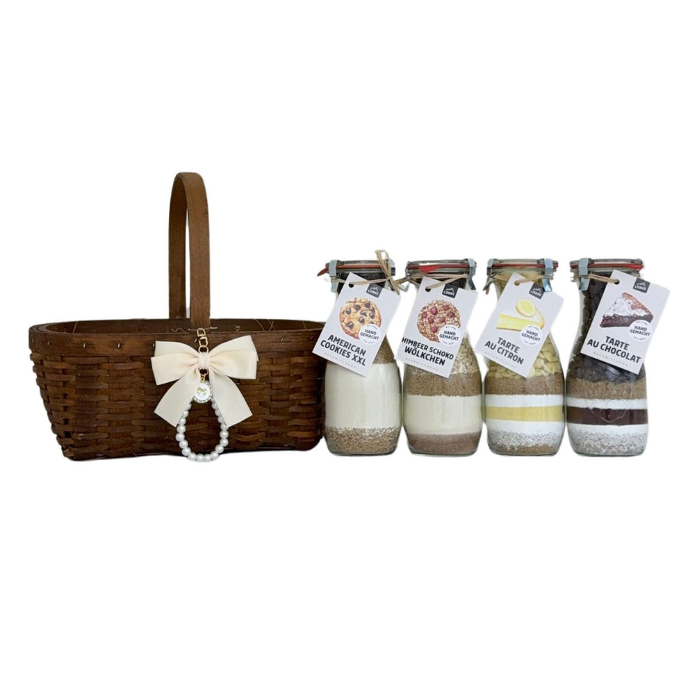 Vier Backmischungen im Glas stehen nebeneinander neben einem dekorativen Korb mit Schleife.