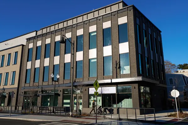 Wide streetscape view of a contemporary mid-rise building with dark gray Iron Rock thin brick, vertical window bays accented by lighter Vesteros Wall thin brick, and ground-floor retail.