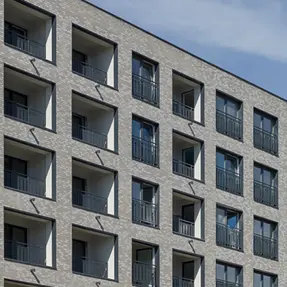 Detailed view of square balcony openings framed in light gray brick with dark metal railings, emphasizing the building’s geometric facade pattern.