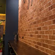 Interior café wall featuring thin brick in warm red and brown tones, installed in a running bond pattern above a long wooden counter with stools and industrial pendant lighting.