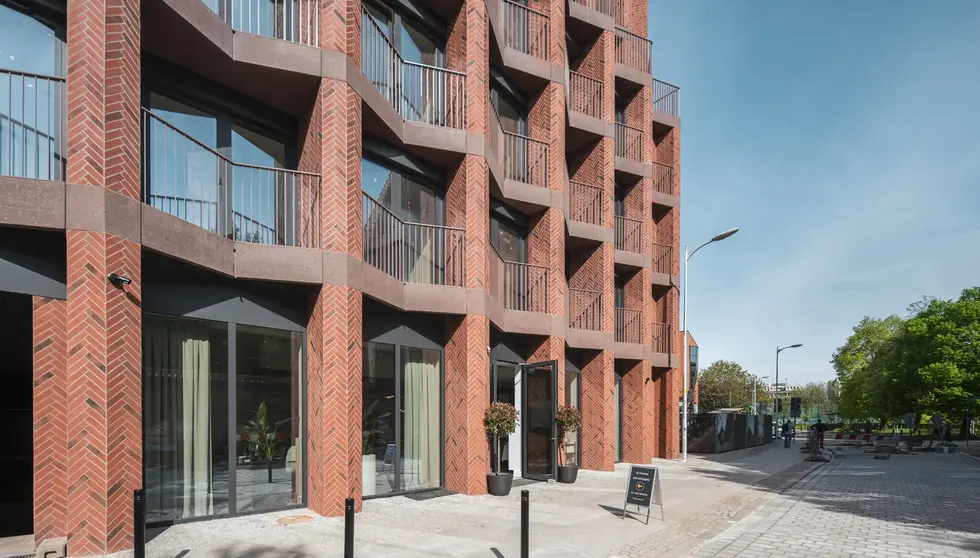 Street-level view of Bernardyńska 4 in Wrocław, Poland, featuring custom red thin brick, deep balconies and geometric detailing.