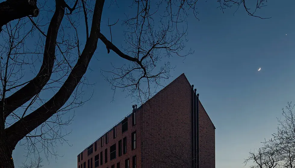 Evening exterior of a residential building finished in Wall Street thin brick in King size, illuminated softly beneath a twilight sky with crescent moon visible.
