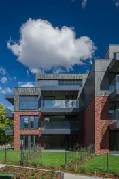 Courtyard view highlighting Gothic Smile and Old Factory king-size thin brick walls framed by landscaped greenery. The brick’s refined texture and horizontal proportions complement the modern architecture and glass balcony details.