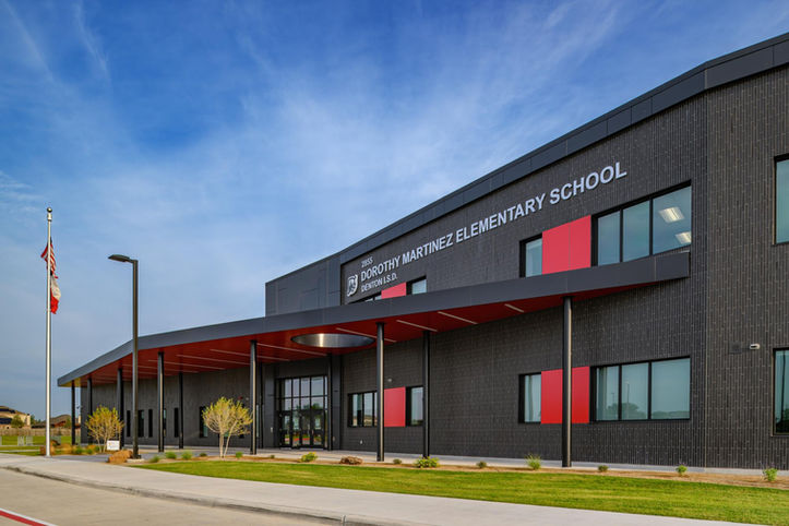 Front entrance of Dorothy Martinez Elementary School in Little Elm, Texas, featuring Black Beauty thin brick in American Imperial size by Acme, with a modern canopy, red accent panels, and contemporary school signage.