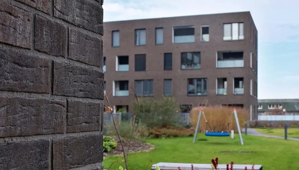 Dark brown residential building finished with Blues Shadow thin brick, overlooking a landscaped courtyard with playground swing and greenery.