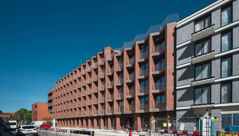 Street view of the Bernardyńska 4 development, featuring custom red thin brick and rhythmic angled balconies.