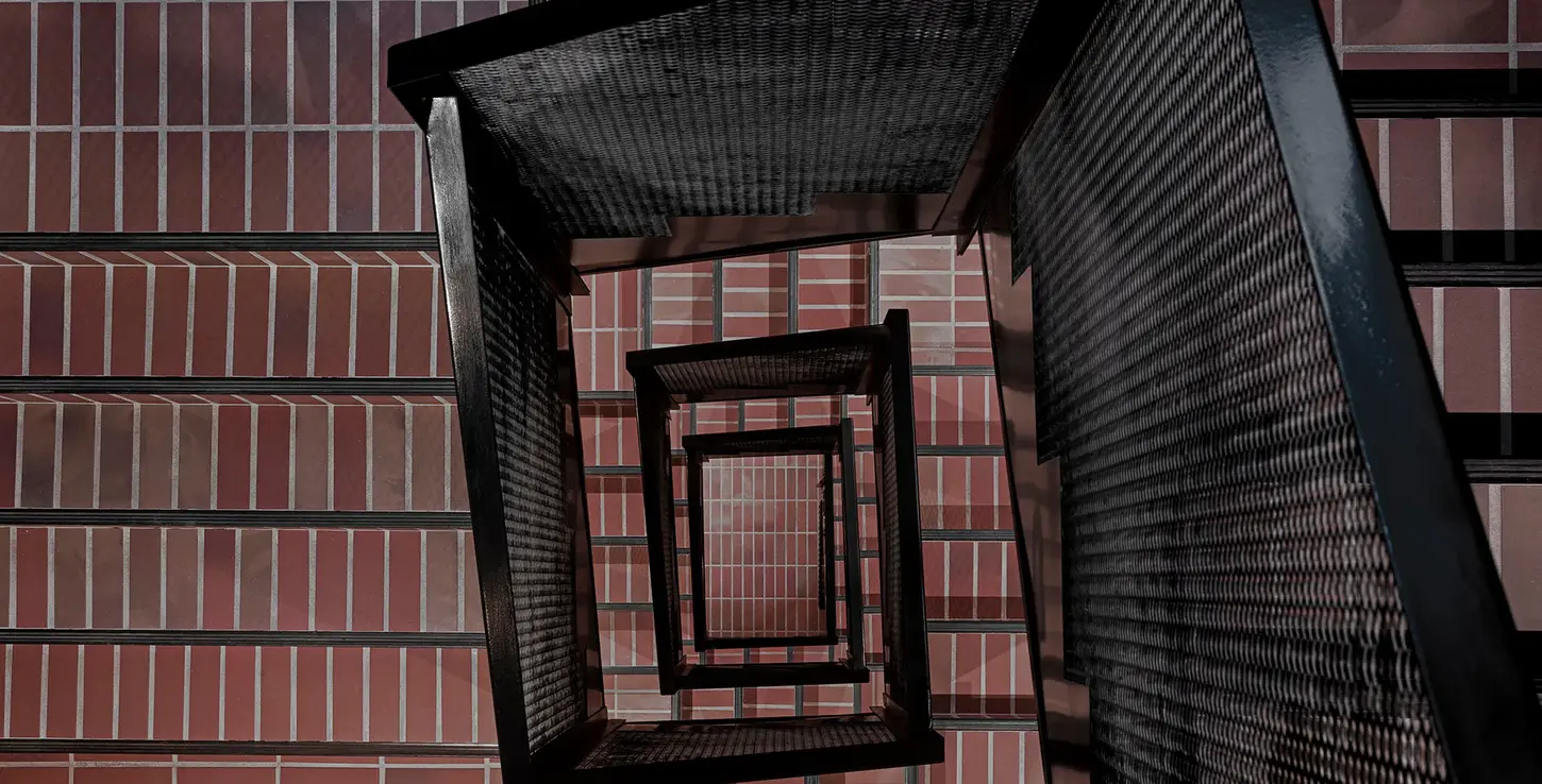 Architectural stair tower view framed by Wall Street thin brick in King size, looking upward through geometric black metal railings with brick walls surrounding.
