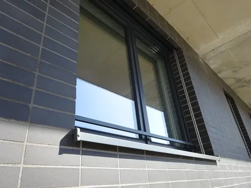 Detail of a window set into dark gray thin brick masonry with horizontal coursing and metal window trim.