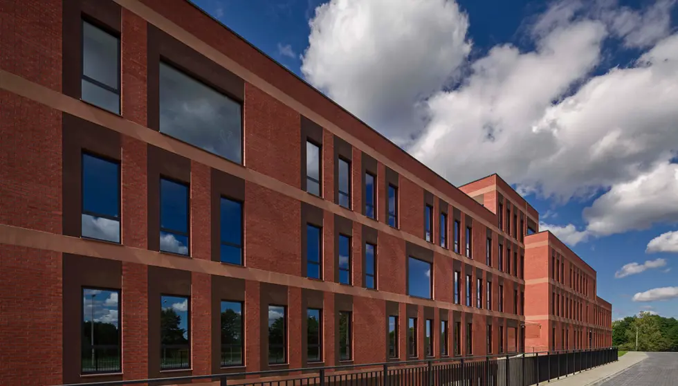 Long exterior view of a university building constructed with Bengali Sunrise thin brick in king size, reflecting blue sky and clouds in large windows and emphasizing the building’s sweeping curved design.