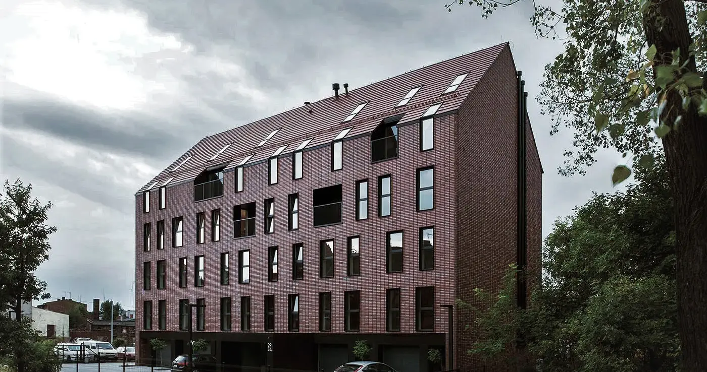 Street-facing perspective of a modern apartment complex clad in Wall Street thin brick in King size, with parked cars and landscaped greenery in the foreground.