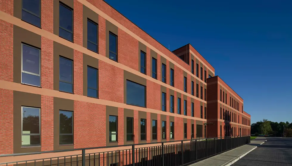 Angled perspective of a modern educational facility featuring Bengali Sunrise thin brick in king size, black metal railing, and strong linear geometry along the facade.