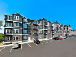 Wide exterior view of a multi-building apartment complex showcasing Blend of 4 thin brick in mixed brown and gray tones, with balconies, parking area, and clear blue sky.