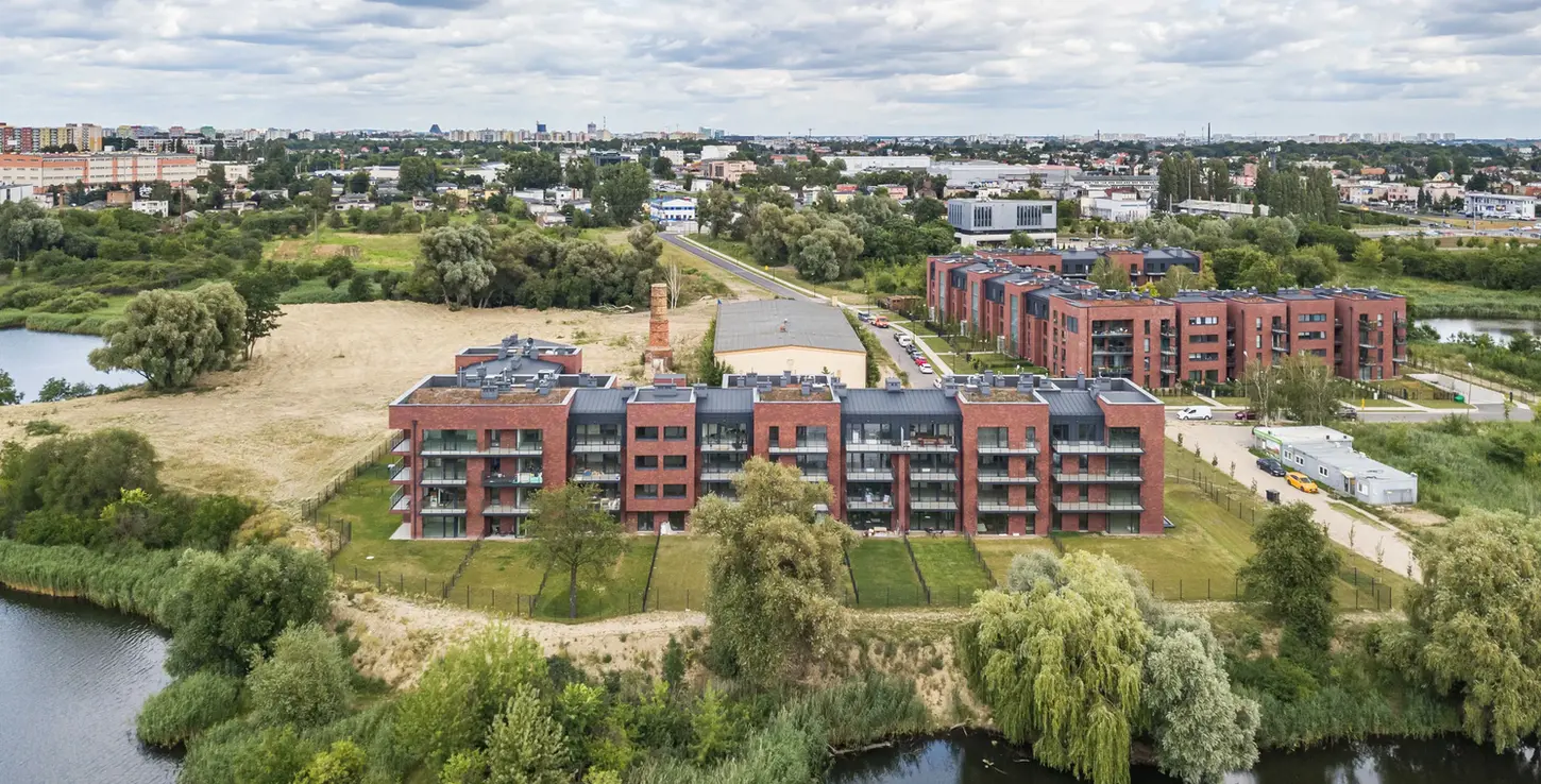 Aerial view of apartment complex finished in Gothic Smile thin brick in king size, set beside a river with surrounding greenery and neighboring residential blocks.