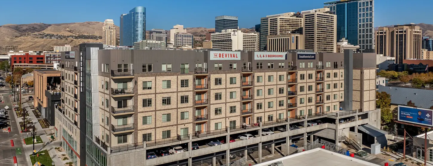Aerial view of The Revival mixed-use apartment building featuring thin brick façades in Roman Theatre, Desert Land, and Manganese, with balconies, integrated parking, and downtown skyline and mountains in the background.