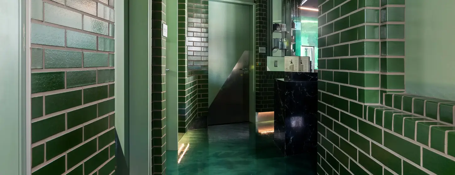 Retail hallway lined with Green Valley Glazed King Size thin brick walls and glossy green finishes at Formula Fig.