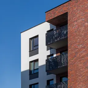 Close-up of apartment balconies against a red brick façade constructed with thin brick blend Red Square, Heart Brick, and Gothic Smile, King 3/8" size, highlighting varied red hues and textured dark accents.