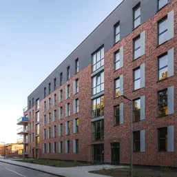 Oblique architectural view of the apartment exterior finished in Old Factory thin brick in King Size, emphasizing the linear window grid and modern gray top level.