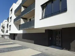 Street-level perspective of a contemporary apartment facade with white exterior walls, dark thin brick base, and projecting balconies with metal railings.