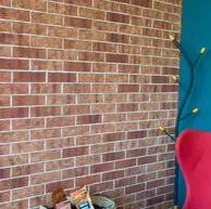 Close-up of a textured thin brick wall in warm red and golden brown shades, paired with a teal accent wall and modern seating in a cozy café setting.