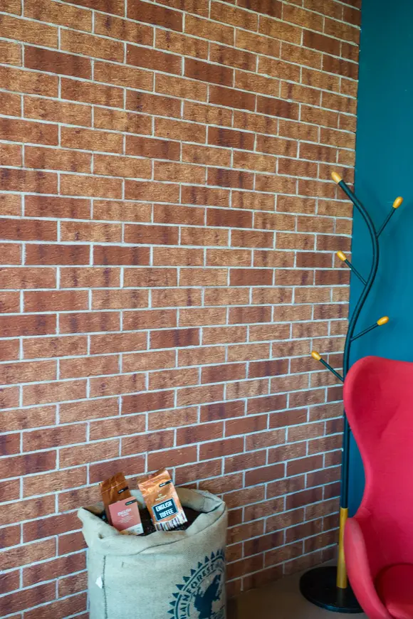 Close-up of Radiant Sunset thin brick in king size, highlighting its textured surface and warm red and golden brown color variation, paired with a teal accent wall in a cozy café setting.
