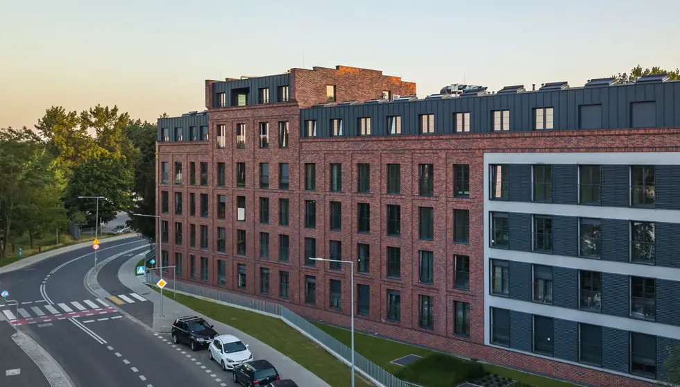 Aerial view of a red brick residential building with dark metal upper stories along a curved urban street.