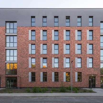 Front elevation of a multi-story apartment building clad in Old Factory thin brick in King Size, highlighting a rhythmic window pattern with subtle dark accents within the red brick façade.