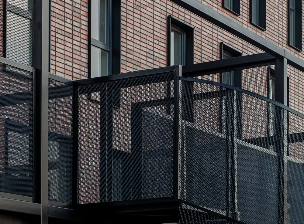 Close-up of metal balcony and staircase structure mounted to a Wall Street thin brick in King size façade, emphasizing texture contrast between brick and black steel mesh.