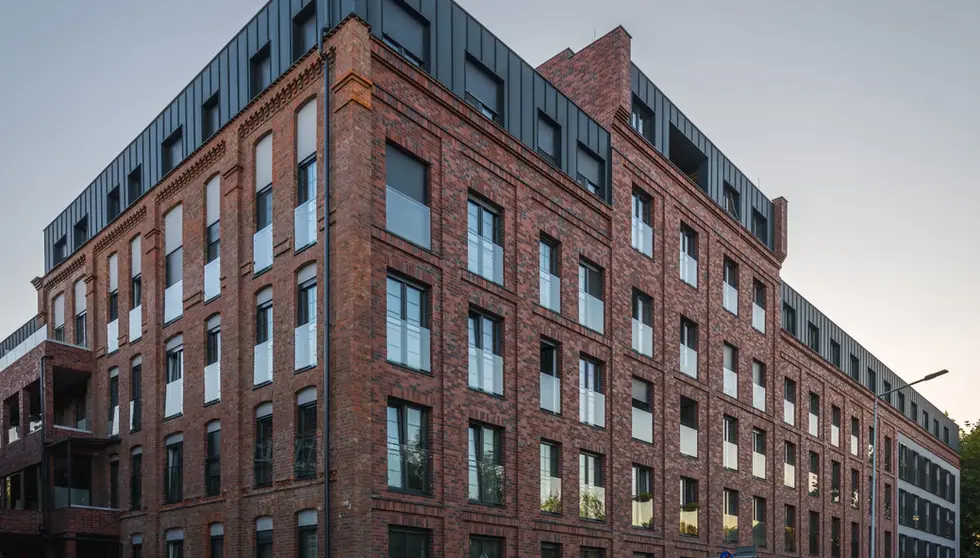 Corner view of a red brick multifamily building with decorative masonry, dark windows and black metal upper floors.
