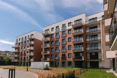 Street-level view of mid-rise residential buildings with red brick facades, white upper volumes, and glass-railed balconies arranged around a landscaped courtyard.
