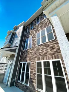 Upward corner view highlighting Blend of 4 thin brick with alternating brown and beige hues beneath dark gray horizontal siding and white trim.