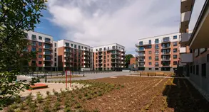 Wide view of a residential complex courtyard framed by red brick apartment buildings with repeating balconies, walkways, and newly planted landscaping.