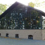 Exterior view of a restaurant pavilion with a gabled glass facade and a base of Aztec Ghost thin brick, featuring light gray and beige tones that blend with the surrounding trees and landscape.