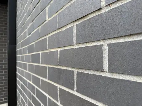 Detailed perspective of dark gray thin brick masonry highlighting linear brick pattern, clean mortar joints, and a black metal corner trim.