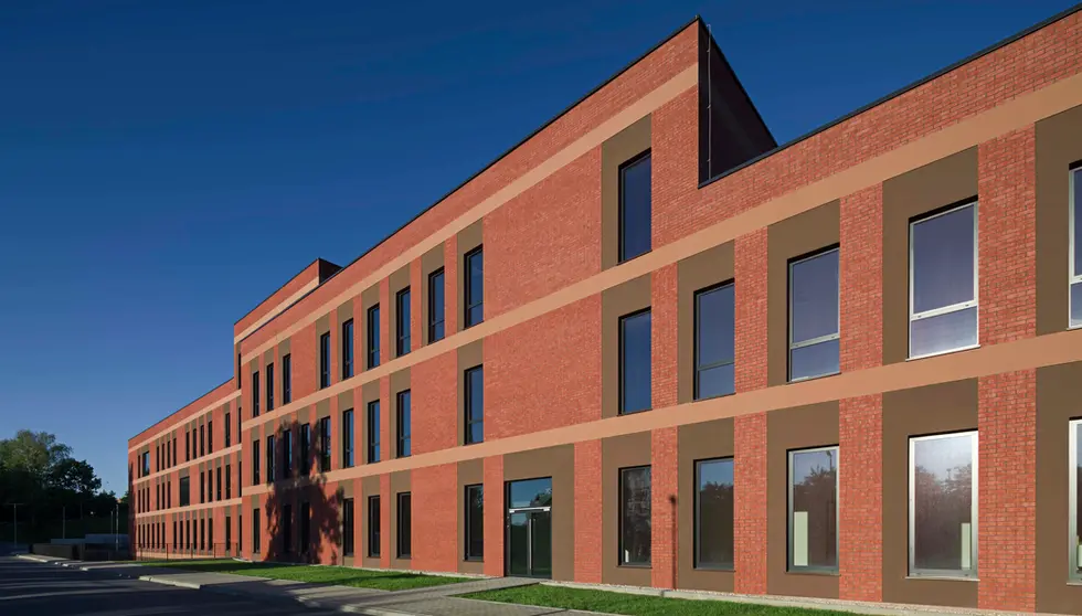 Angled view of university facade built with Bengali Sunrise thin brick in king size, highlighted by rhythmic vertical window openings and warm red brick texture under a clear blue sky.