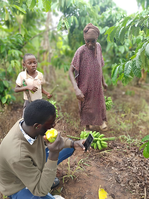 Man eats fruit, photographs bananas with phone; woman, child in background