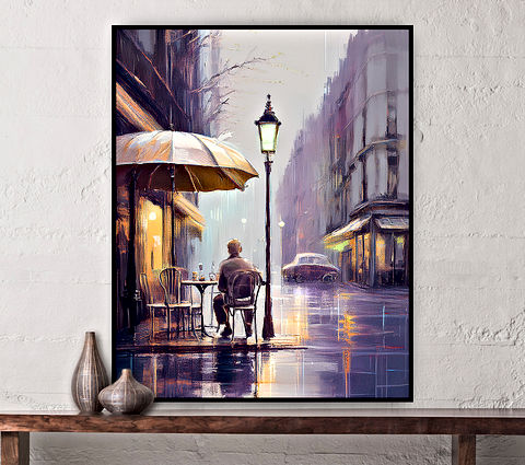 The image depicts a street scene on a rainy day. A person is sitting at a table under a large yellow umbrella, facing away from the viewer. The street is lined with buildings and a lit street lamp. The wet pavement reflects the lights and colors around, suggesting recent rain. A car is visible in the background, its form blurred. The scene evokes a sense of solitude and quietness in an urban setting.