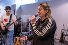 A singer performs with joyful focus during an open mic night at Chorus Studio in Vancouver, backed by a live guitarist and cozy studio setting.
