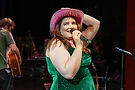 Chorus Studio karaoke night with a bold performer singing in a cowboy hat, dramatic stage makeup, and vibrant dress, bringing flair and fun to the mic.