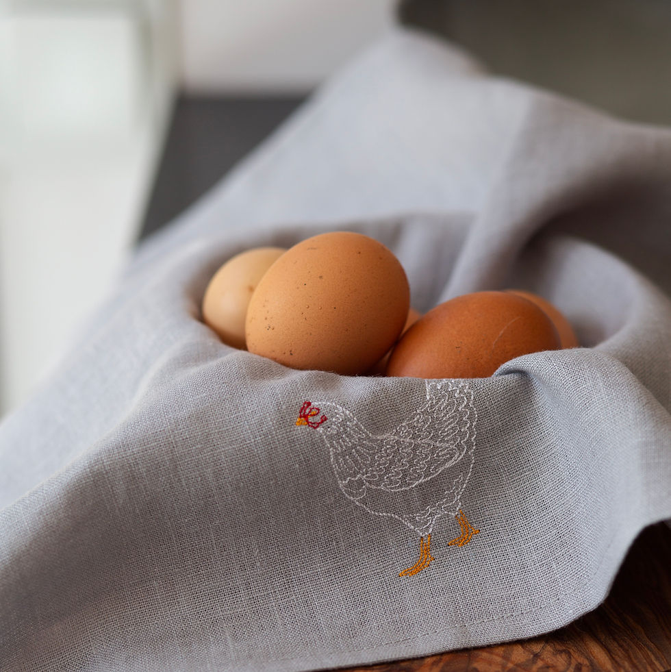 Hellgraue Leinenserviette mit Welsumer-Huhnstickerei in einem Korb mit frischen Eiern