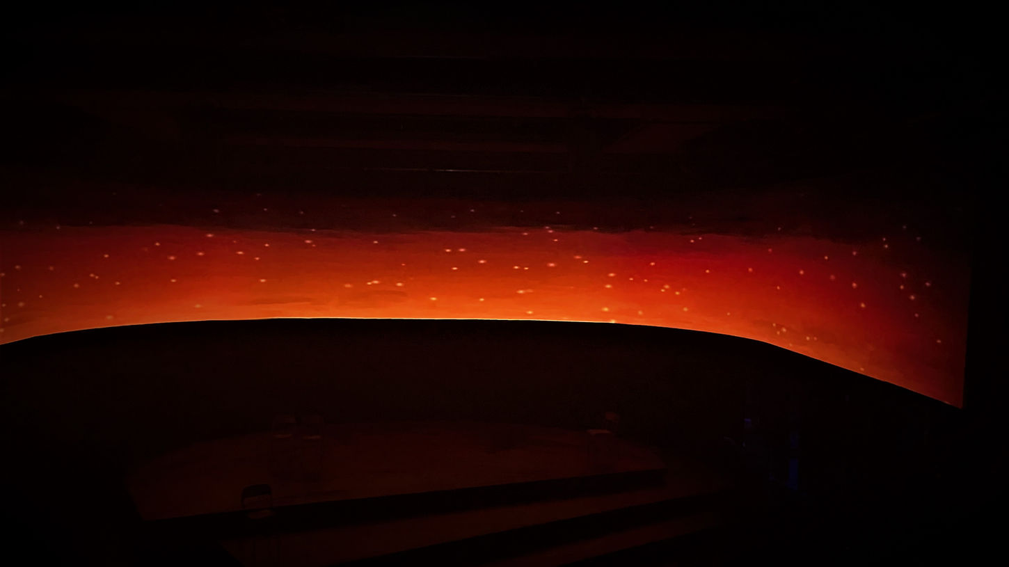 A large, curved projected image of a dark orange sunrise fading out the night sky.