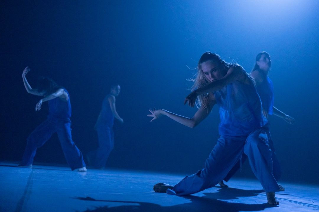 Four performers, mid-pose, dressed in blue. They are lit in blue.