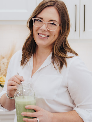 Candace with medium length brown hair, glasses, wearing white button-down blouse, standing while holding a green smoothie in a mason jar